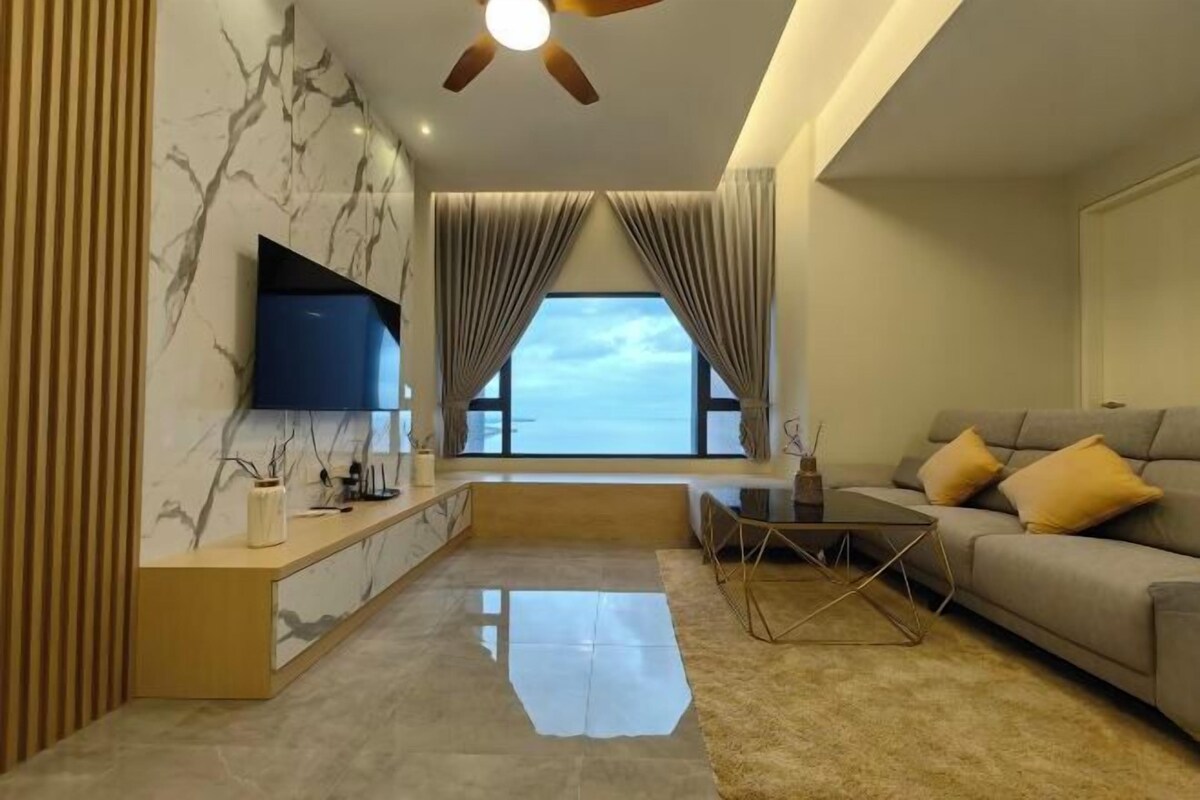 A modern living room with a sofa, a coffee table, a TV mounted on the wall, and a window with curtains.