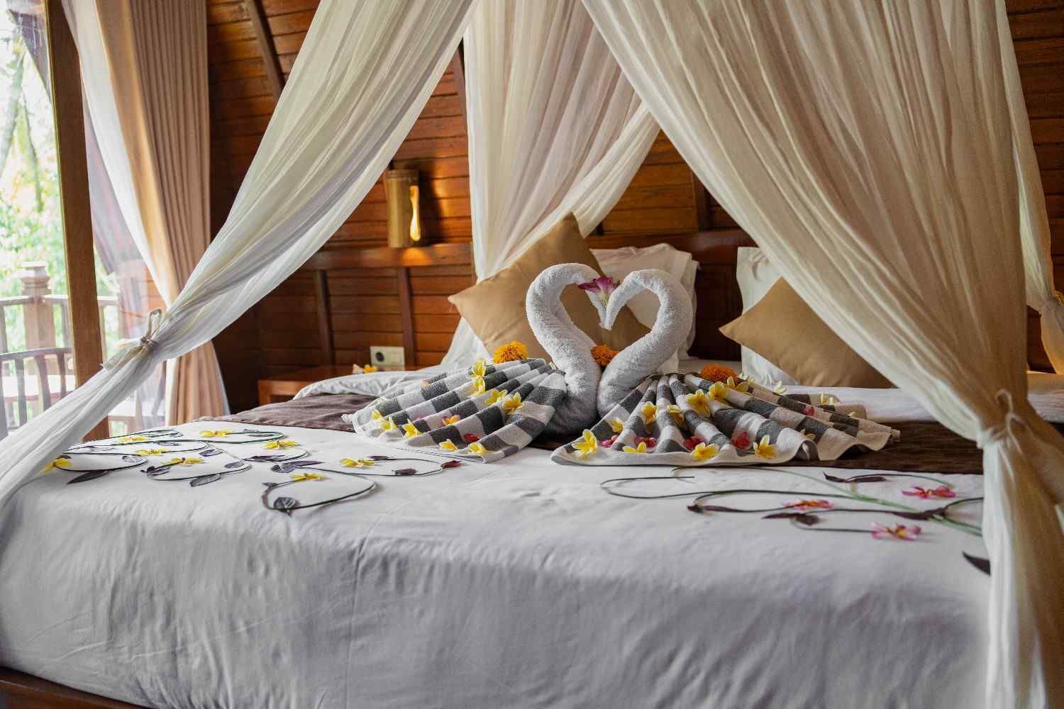 A bed with a canopy, swan-shaped towels, and a checkered blanket.