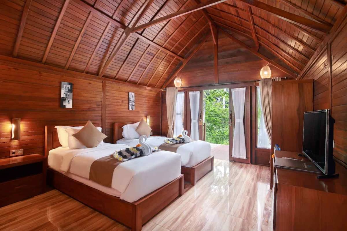 A wooden cabin-style room with two beds, a flat-screen TV, and a large window with curtains.