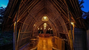 An interior view of a bamboo structure with a central chandelier, wooden flooring, and a bar area. - Bila Penida Resort & Farm (Penida Island)