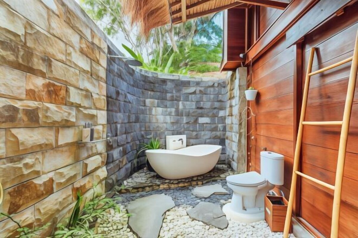 A bathroom with a stone wall, a bathtub, a toilet, and a wooden door.