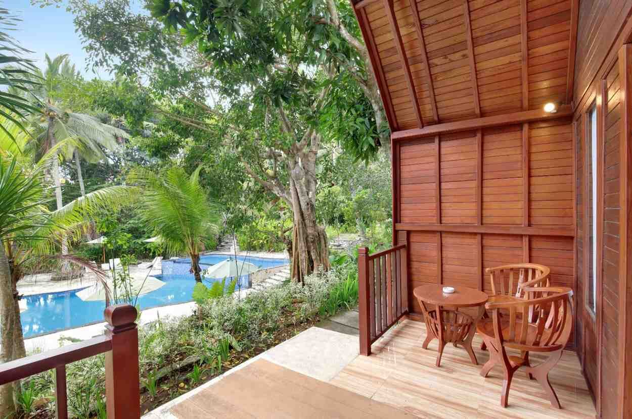 Terraza de madera con vista a una piscina, rodeada de exuberante vegetación.