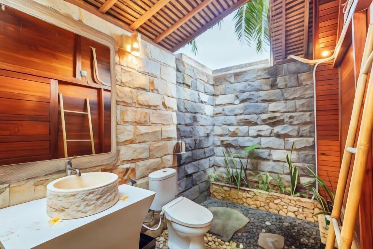 A bathroom with a stone wall, wooden cabinets, a sink, and a toilet.
