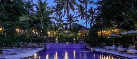 A pool area with palm trees, lounge chairs, and a stone wall.