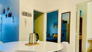 A modern dining area with a round table, white chairs, and a stainless steel kettle.