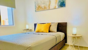 A neatly made bed with a patterned bedspread, two bedside lamps, and a painting on the wall.