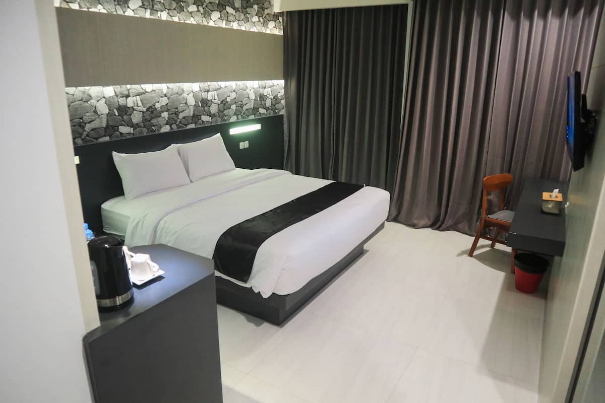 Ein Hotelzimmer mit einem Bett, einem Schreibtisch mit Telefon, einem Sessel, einem Fernseher und einer Steinwand.