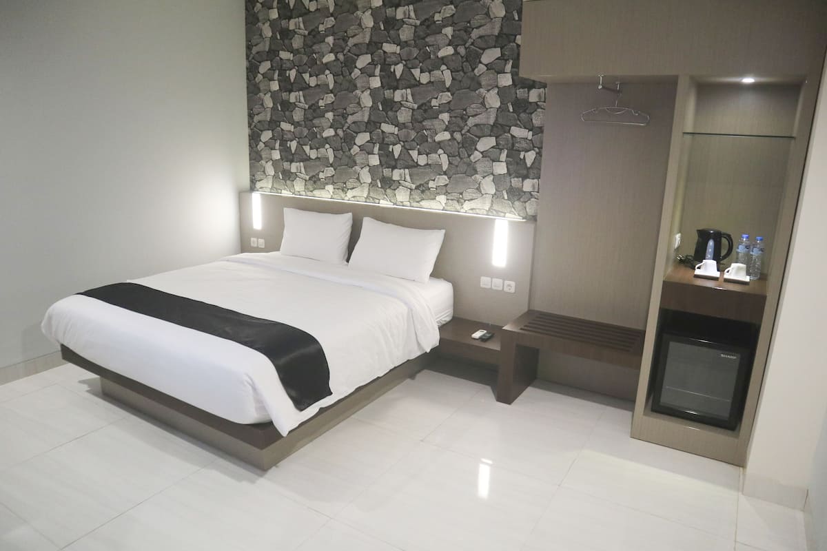 Ein modernes Hotelzimmer mit einem großen Bett, einer integrierten Heizung, einem kleinen Tisch mit Telefon und einer Kaffeemaschine.