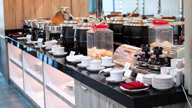 A buffet setup with various food containers, serving dishes, and utensils. - LEX HOTEL BANJARMASIN BY EXCELSIOR (Banjarmasin)