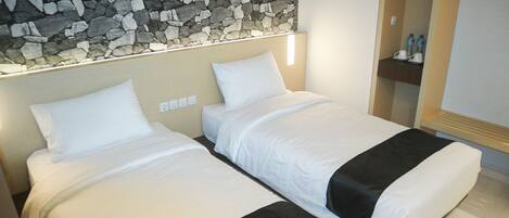 A hotel room with two beds, a stone wall, a wooden shelf with water bottles, and a mirror.