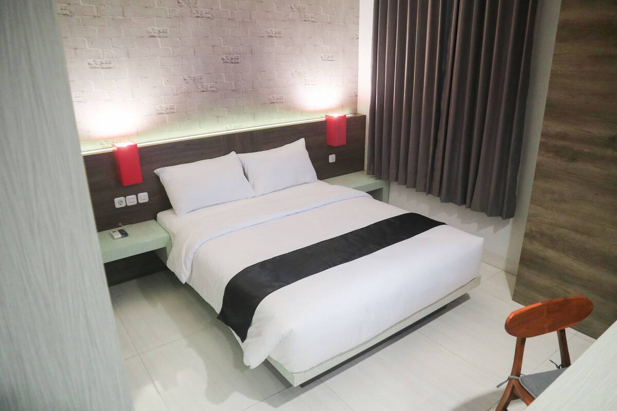 Ein Hotelzimmer mit einem Bett, Nachttischen, einer roten Lampe und einem Holzsessel.