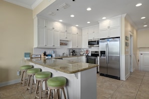 A kitchen with white cabinets, a stainless steel refrigerator, a microwave, and a granite countertop. There are four green stools at the island.