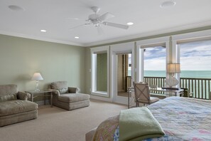 A hotel room with a bed, two armchairs, a small table with a lamp, and a view of the ocean through a balcony.
