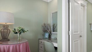 A room with a round table, a lamp, a vase with flowers, a dresser, a mirror, and a door.