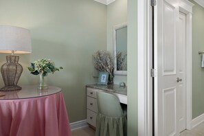 Une pièce comprenant une table ronde, une lampe, un vase avec des fleurs, une commode, un miroir et une porte.