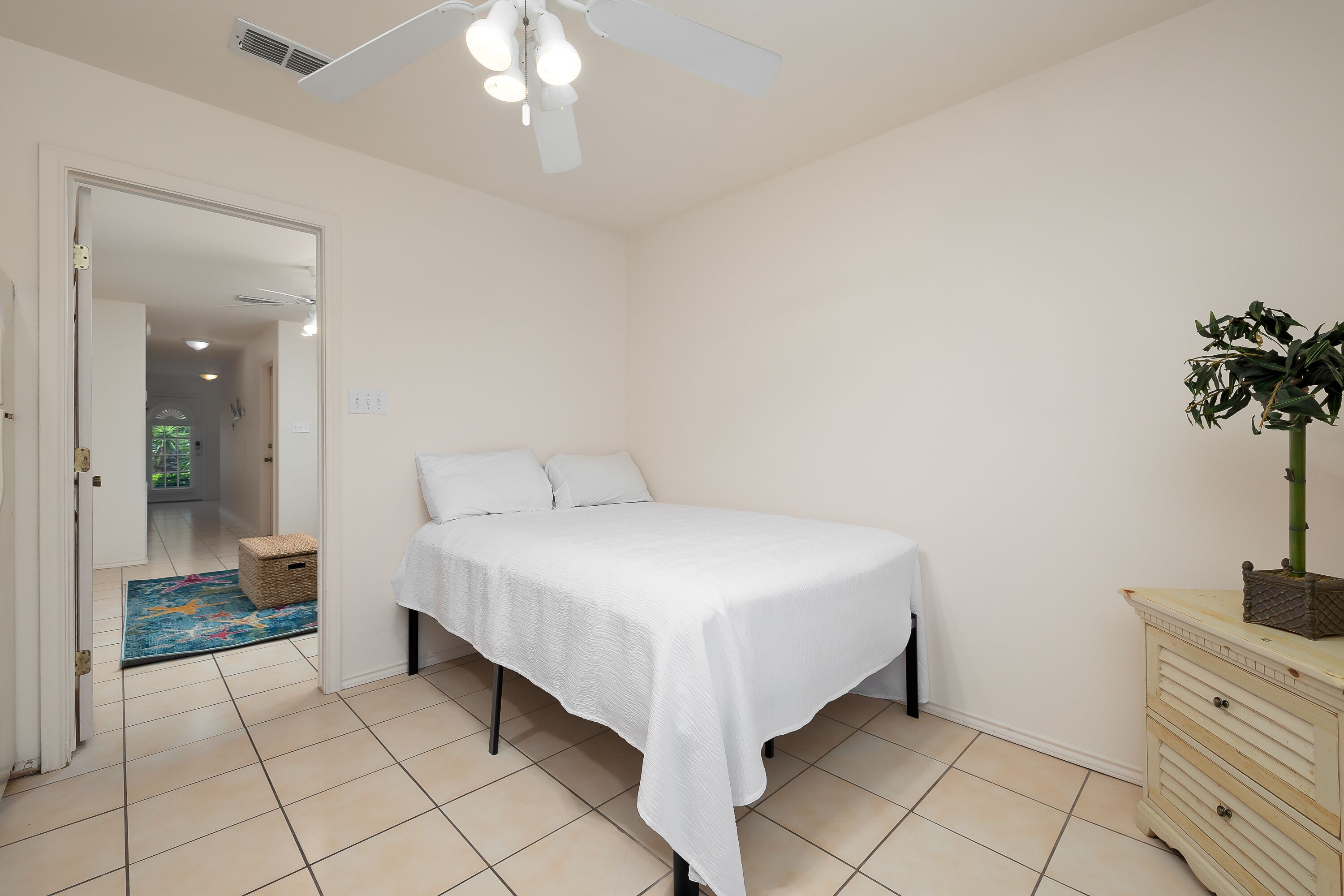 Un dormitorio con una cama, un aparador, un ventilador de techo y una puerta que da a otra habitación.