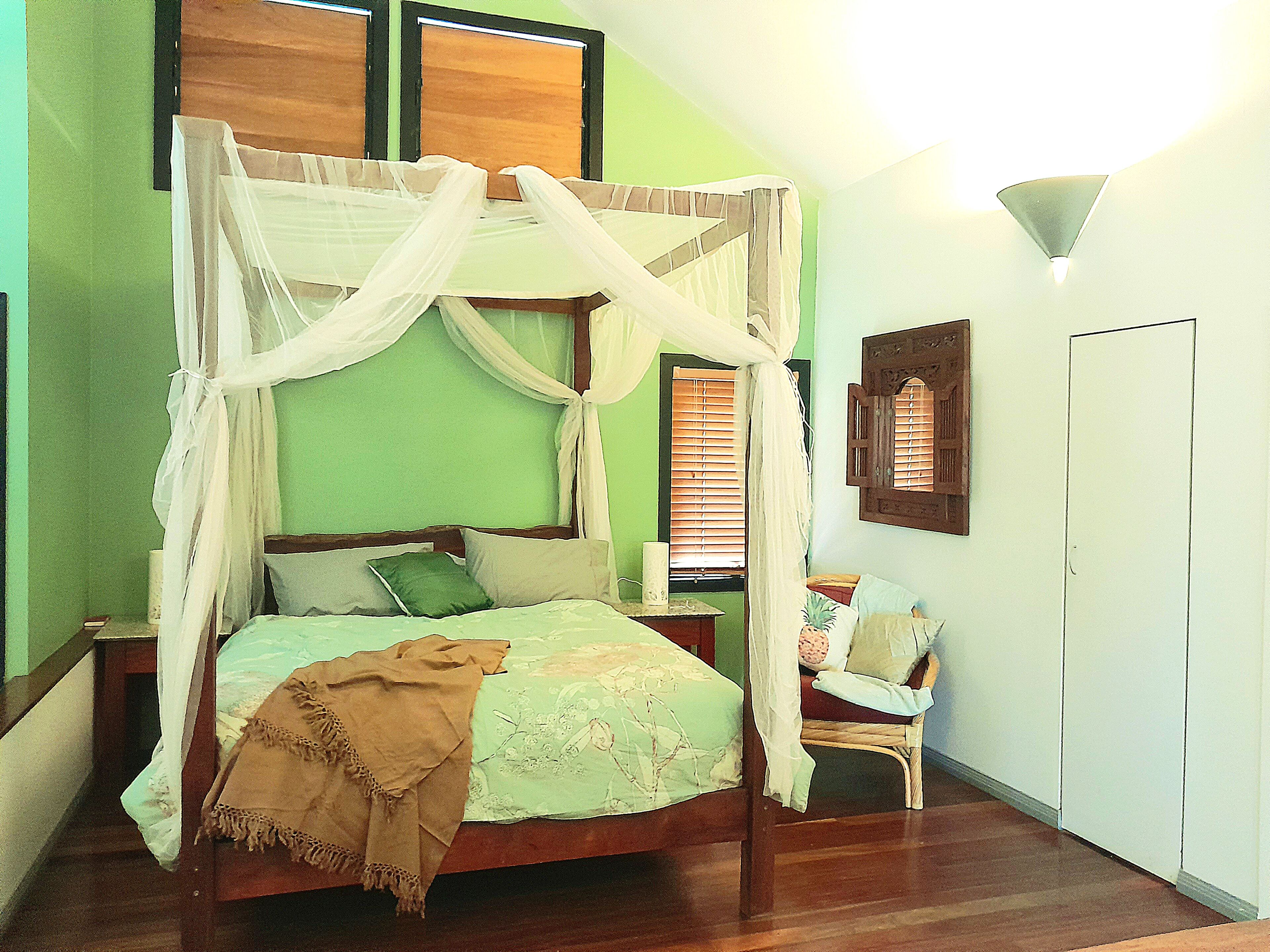 Una cama con dosel sobre cuatro columnas con estructura de madera, pared verde y suelo de madera.