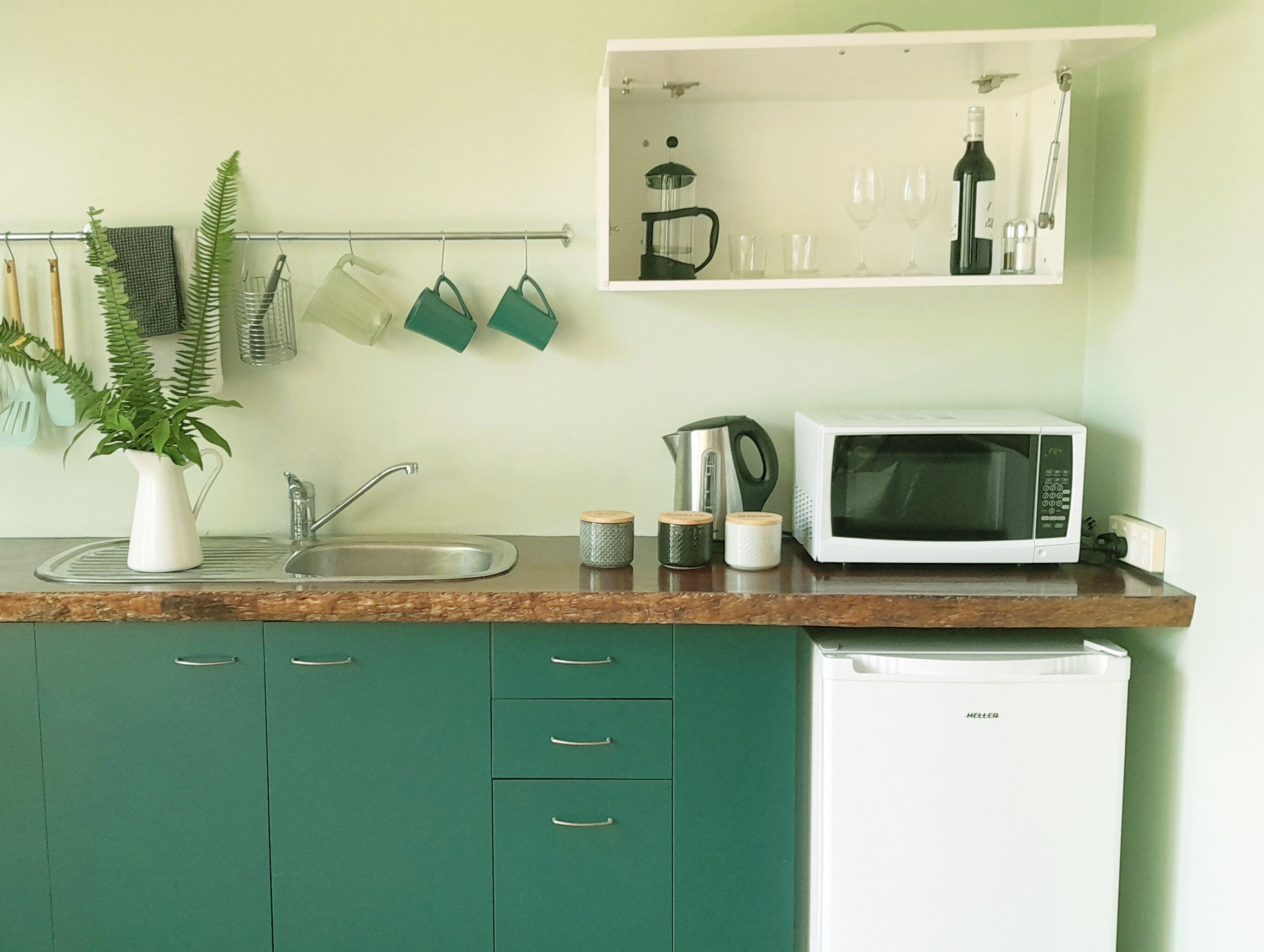 A kitchen with a sink, a microwave, a kettle, and a cabinet.