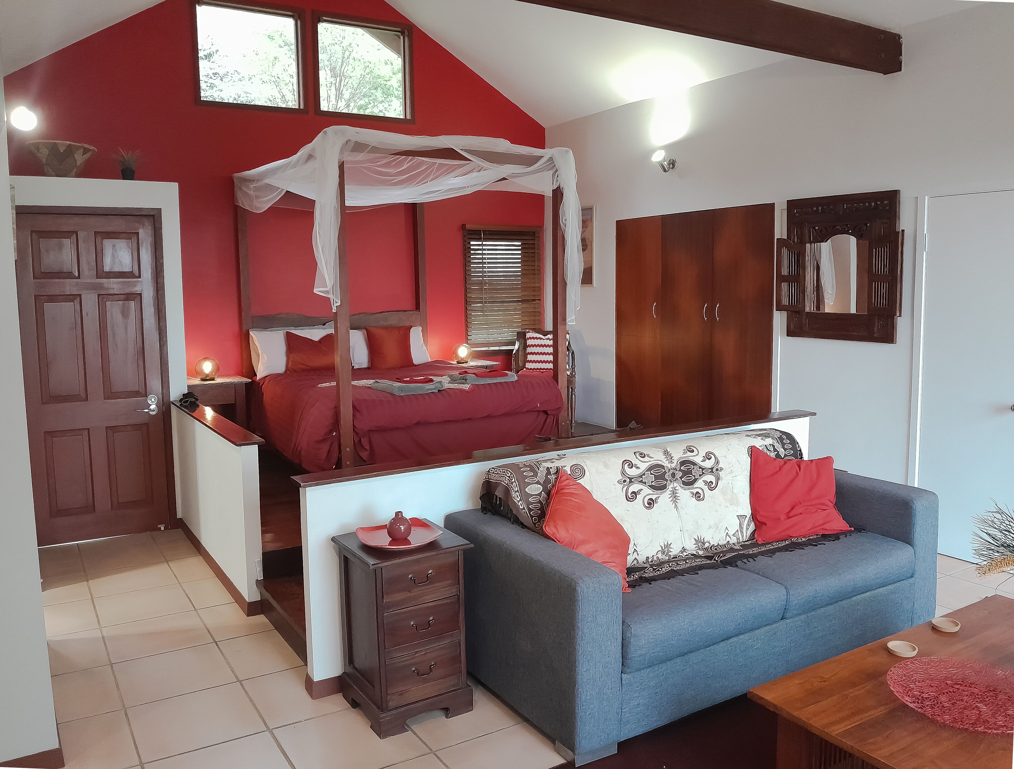 Un dormitorio con una cama con dosel, un sofá, un armario de madera y un guardarropa.