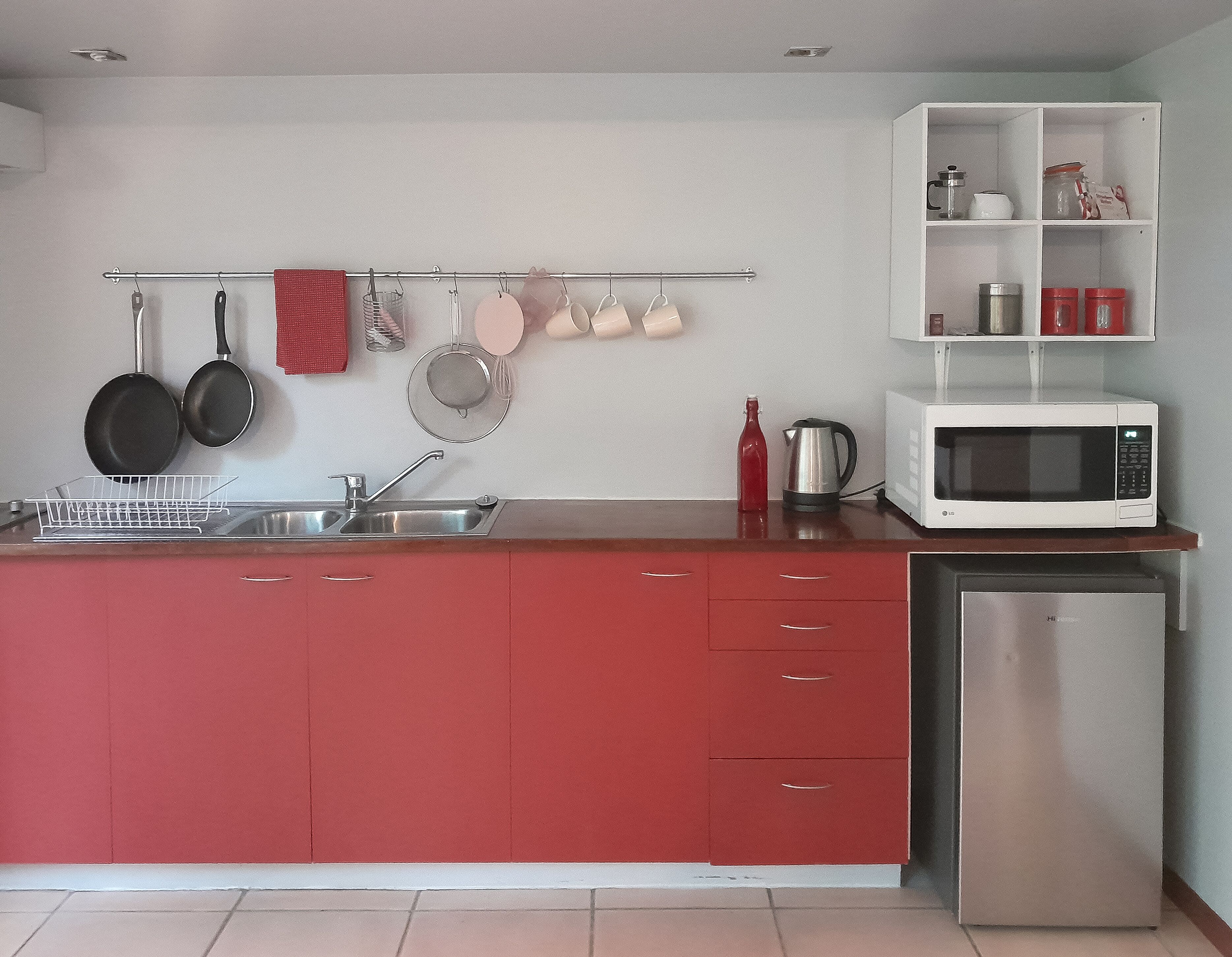 Una cocina compacta con un lavamanos de acero inoxidable, un microondas blanco y un refrigerador rojo.