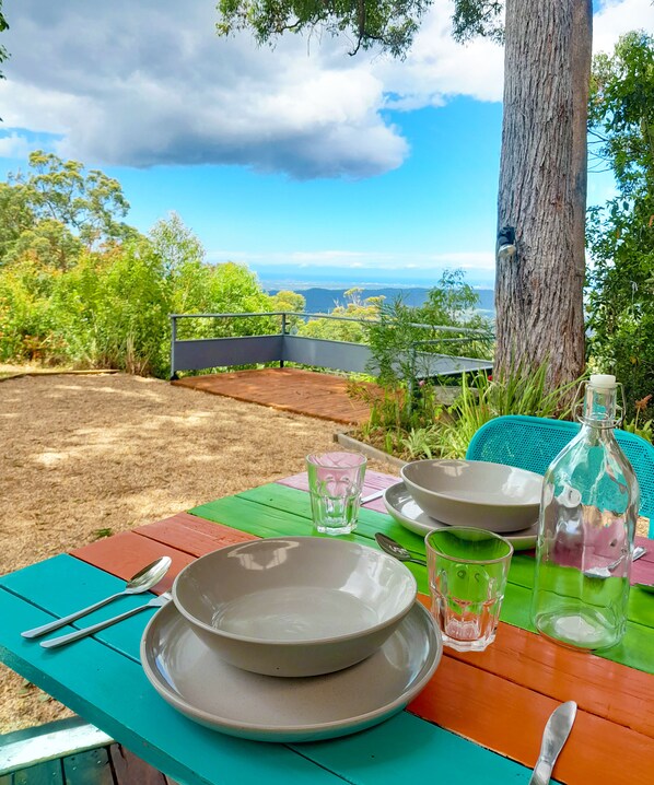 A dining table set outdoors with a scenic view, including a tree and a metal railing. - Sky Island Studios (Clagiraba)