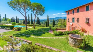 Una casa con piscina, un pozo de piedra y un jardín con árboles y arbustos.