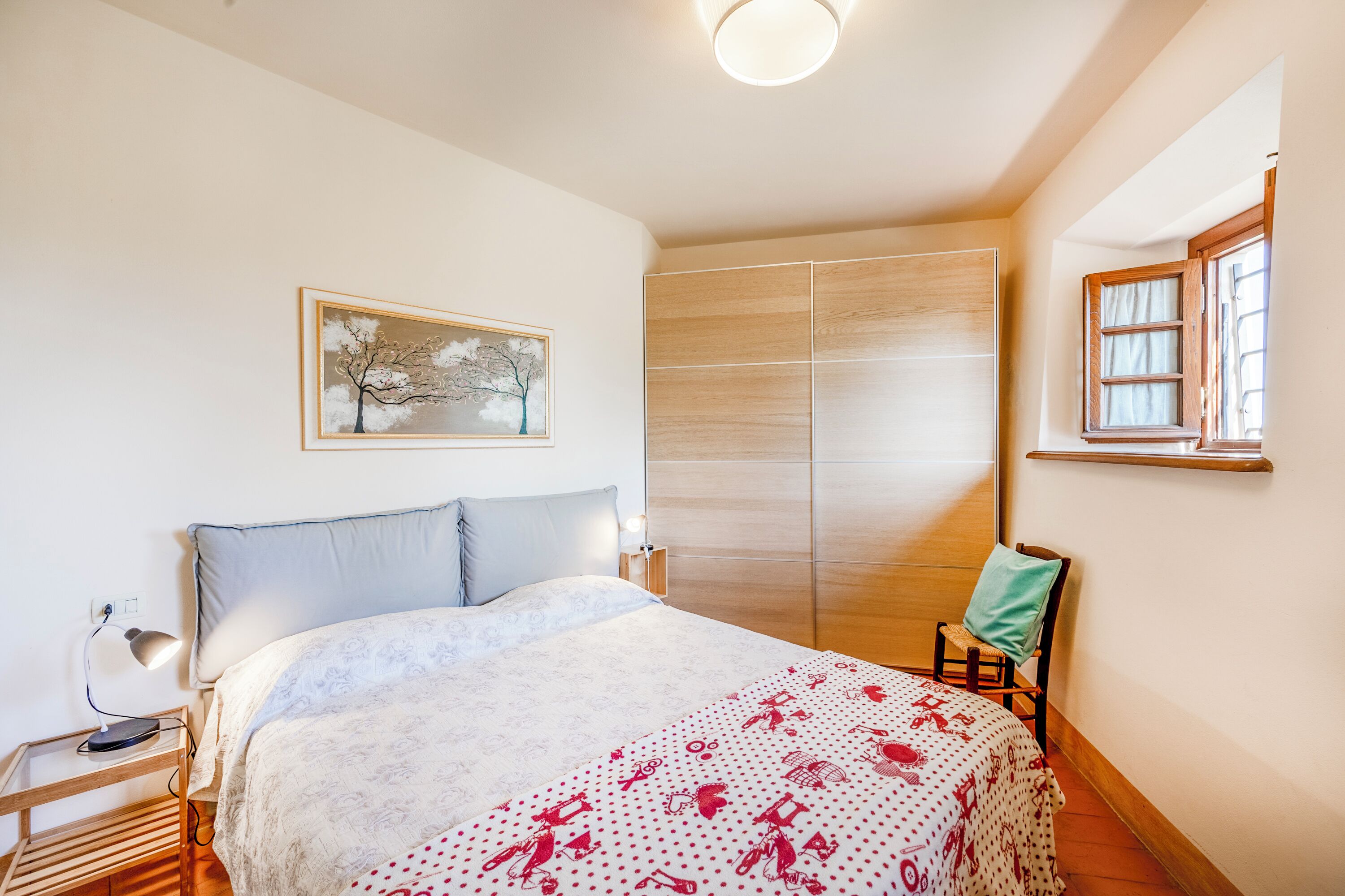A bedroom with a bed, a nightstand, a chair, a wardrobe, and a window.
