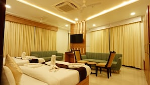 A hotel room with a large bed, two green sofas, a TV mounted on the wall, and a ceiling fan.