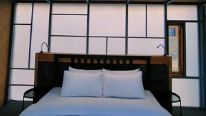 A modern hotel room with a large bed, wooden headboard, and a view through the window. - The Merak (Leh)