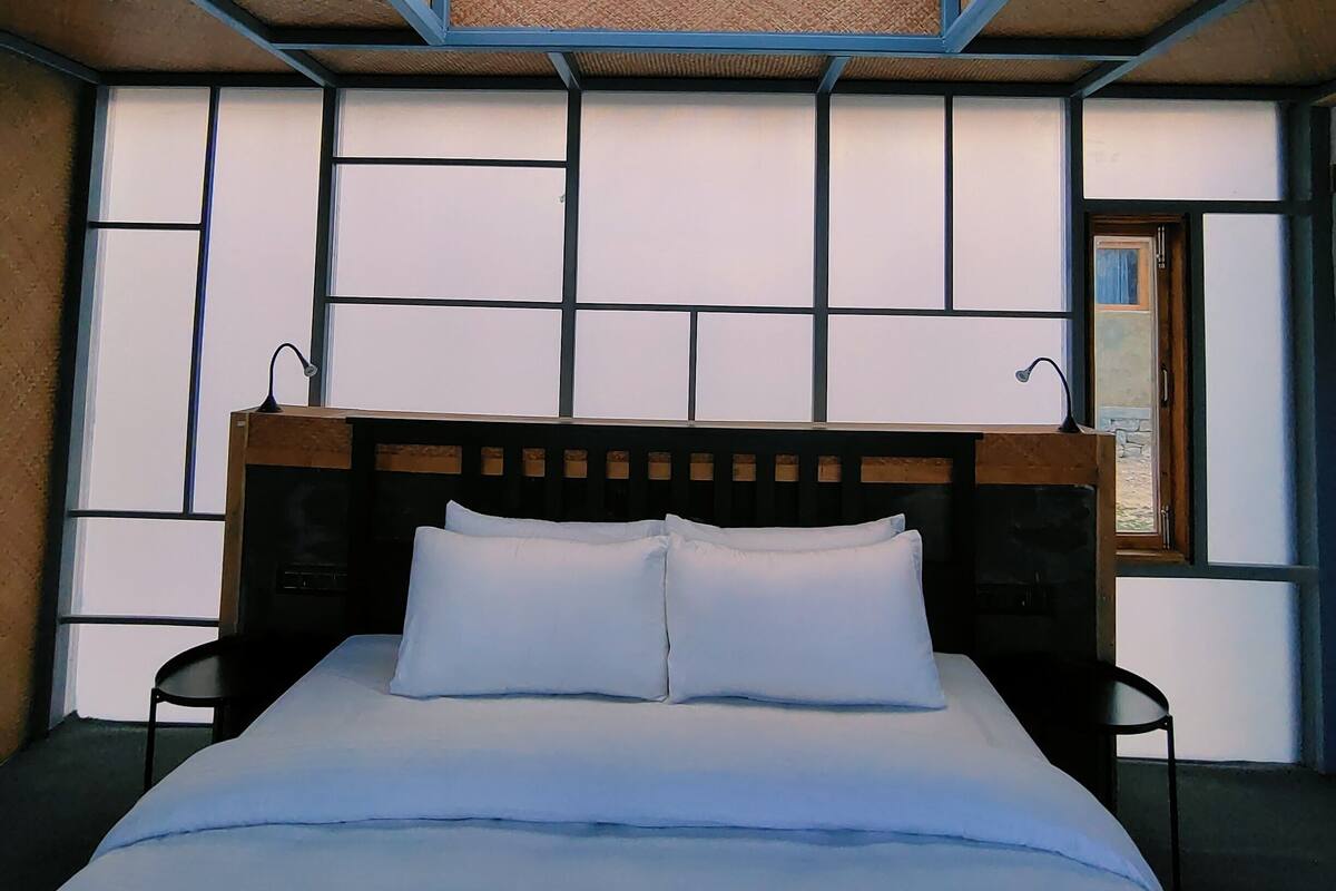 Una habitación de hotel moderna con una cama grande, cabecero de madera y vistas por la ventana.