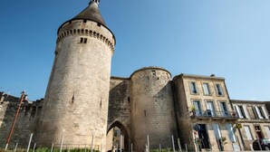 A historic stone tower with a conical roof, adjacent to a multi-story building with windows and balconies. - Logis Hotel de la Tour (Libourne)