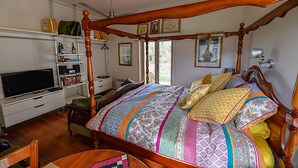 Ein geräumiges Schlafzimmer mit einem großen Bett, einem Holz-Kopfteil und einem Fernseher auf einem Schrank.