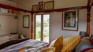 Ein Schlafzimmer mit Himmelbett, Schminktisch, Spiegel und einem Fenster mit Blick ins Freie.
