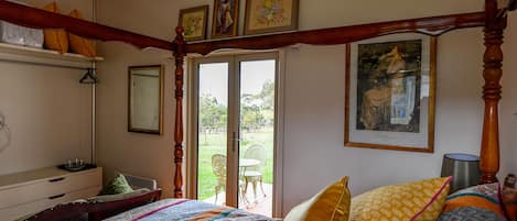 A bedroom with a four-poster bed, a dresser, a mirror, and a window with a view of the outdoors.