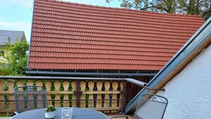 A patio with a round metal table and two chairs, a wooden fence, and a red-tiled roof in the background. - Vacation in the Allgäu, vacation home Dorn (Altusried)