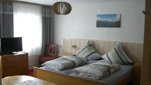A bedroom with a wooden bed, a television on a wooden cabinet, a chair, a bedside table, and a hanging light fixture. - Vacation in the Allgäu, vacation home Dorn (Altusried)