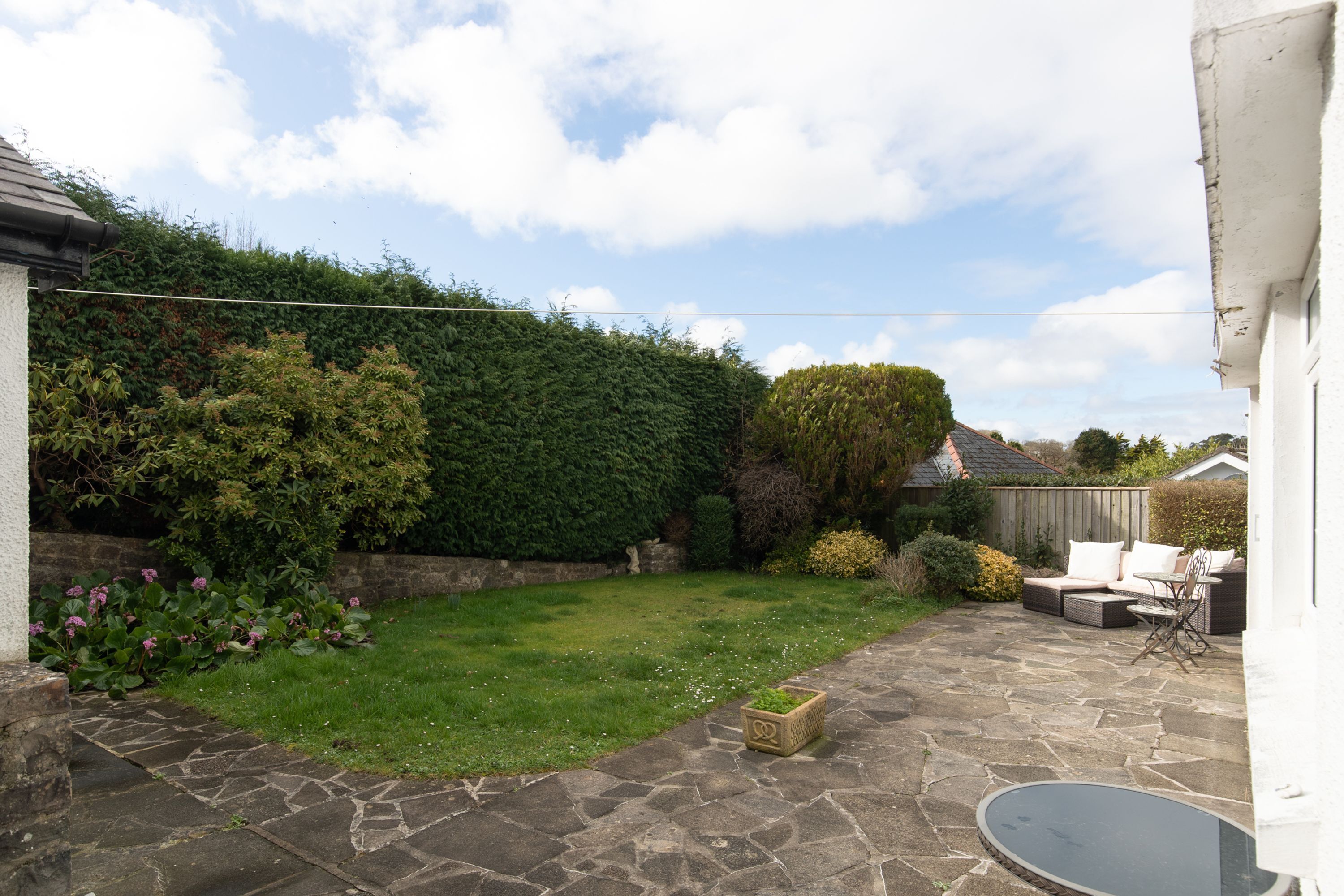 A backyard with a stone patio, a grassy lawn, and a wooden fence.