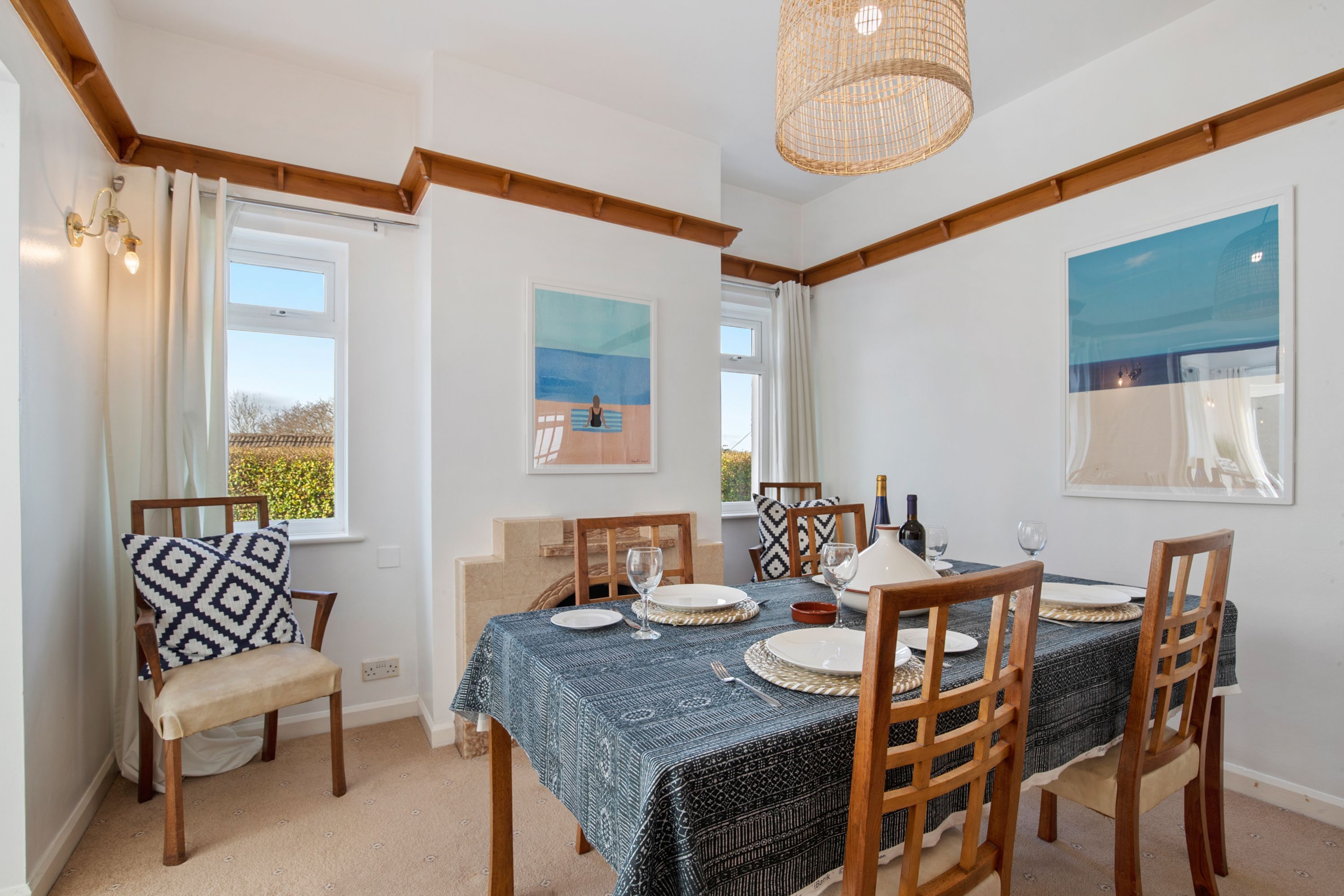A dining area with a table set for six, wooden chairs, a patterned tablecloth, and artwork on the walls.