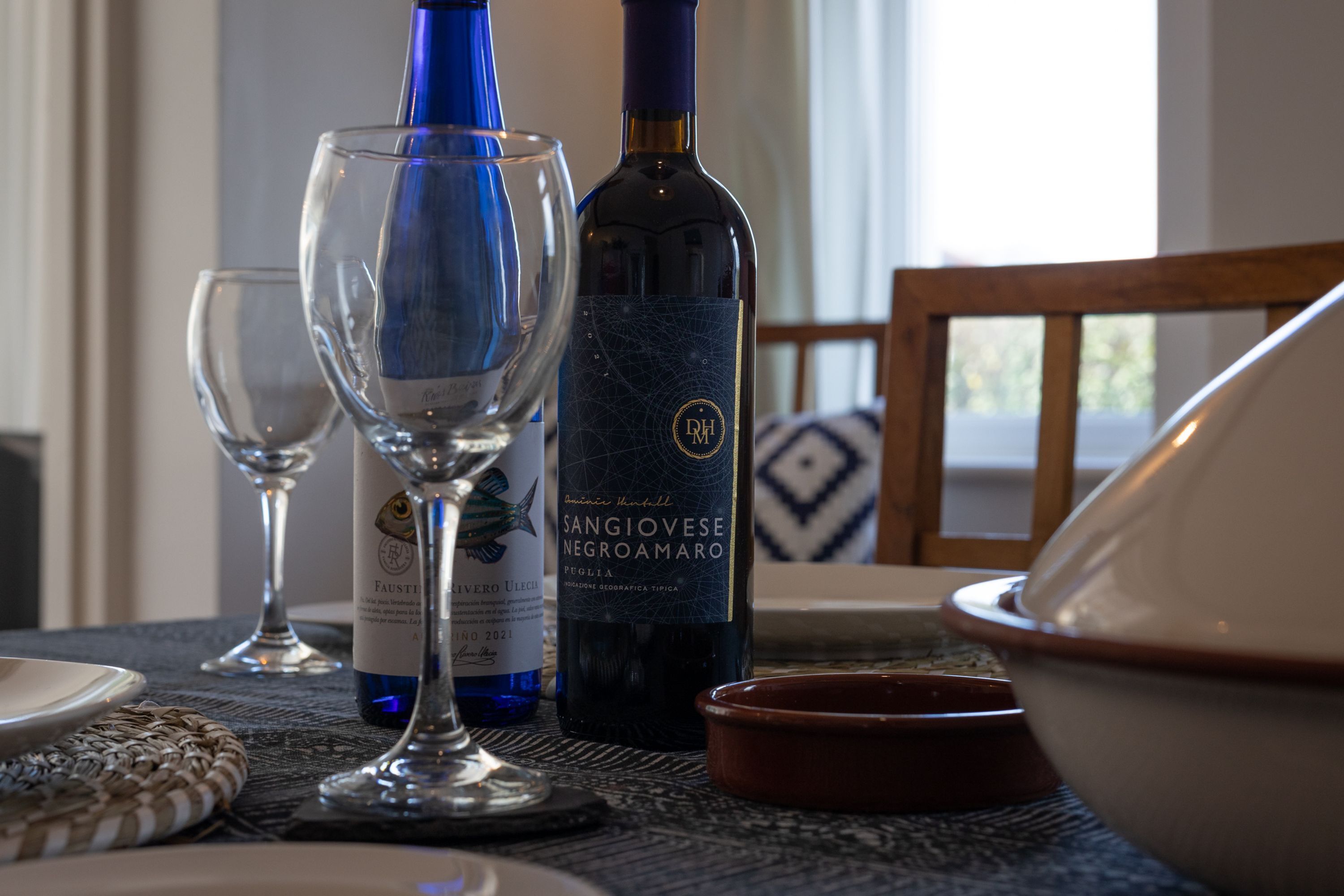 A dining table with a bottle of Sangiovese Negroamaro wine, a wine glass, and a bowl.