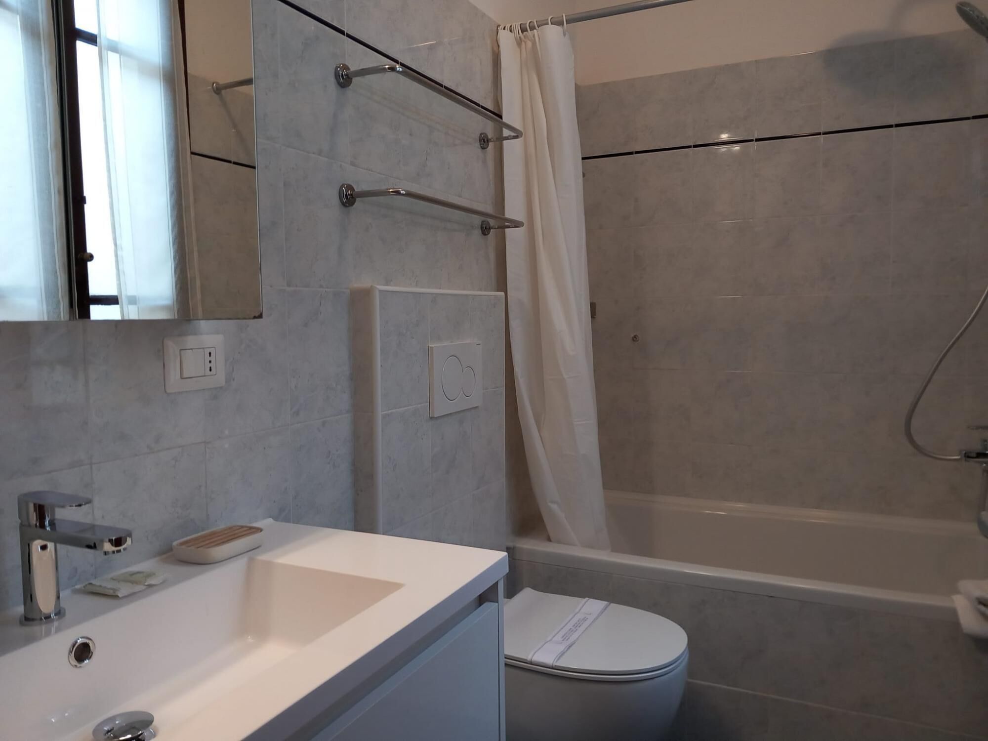 A modern bathroom with a white sink, mirror, and toilet. There is a shower with a glass door and a curtain.