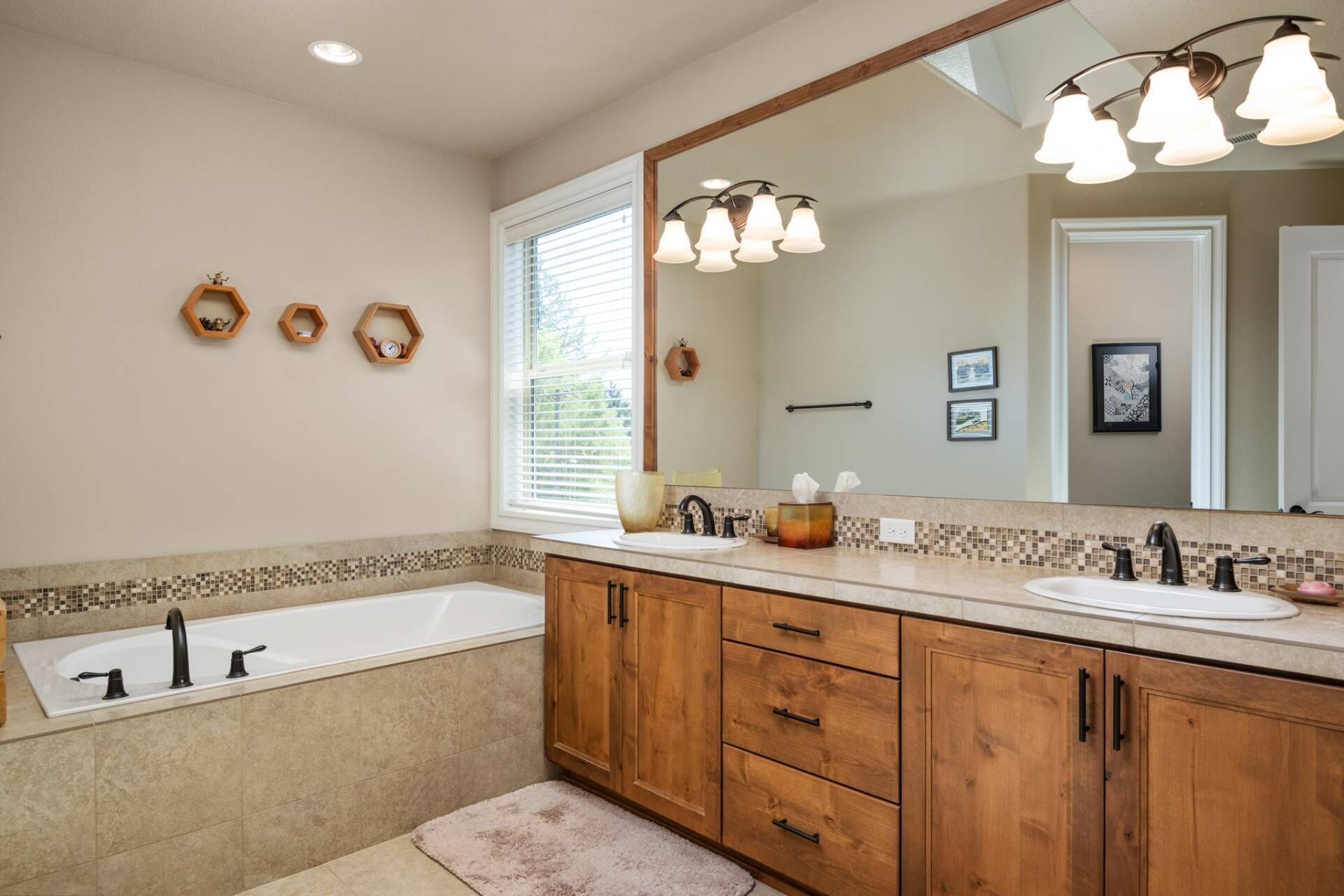 A modern bathroom with a large mirror, wooden cabinets, a bathtub, and a vanity with a sink.