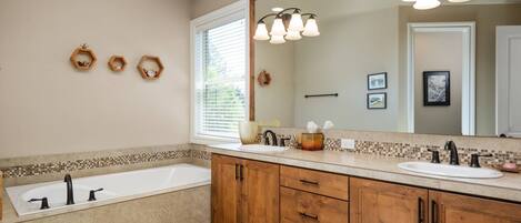 A modern bathroom with a large mirror, wooden cabinets, a bathtub, and a vanity with a sink.