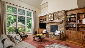 A living room with a stone fireplace, large windows, a bookshelf, and a cozy seating area. - Impeccable Décor and Furnishing, Splendid Neighborhood, Pet Friendly, Fenced Backyard, Next to Park (Portland)
