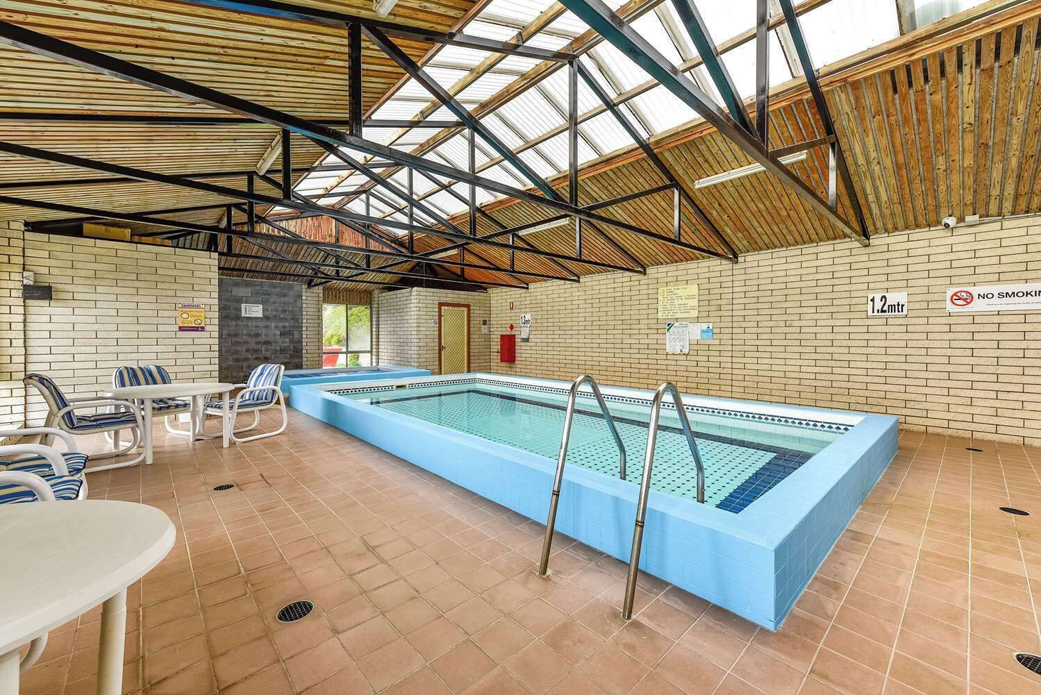 Une piscine intérieure avec un sol carrelé, des échelles en métal et un mur en briques sur lequel est affiché un panneau indiquant « INTERDICTION DE FUMER ».