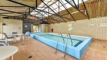 Une piscine intérieure avec un sol carrelé, des échelles en métal et un mur en briques sur lequel est affiché un panneau indiquant « INTERDICTION DE FUMER ».