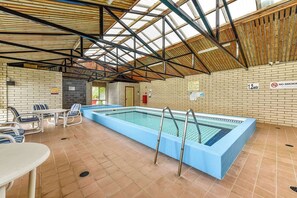 Una piscina interior con suelo de baldosas, escaleras metálicas y una pared de ladrillo con un cartel de 'NO FUMAR'.