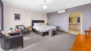 A hotel room with a bed, two armchairs, a small table, a mirror, and a doorway leading to a bathroom.