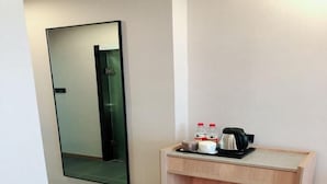 Une chambre d’hôtel avec un grand miroir, une petite table d’appoint en bois, une bouilloire, des tasses et une bouteille.