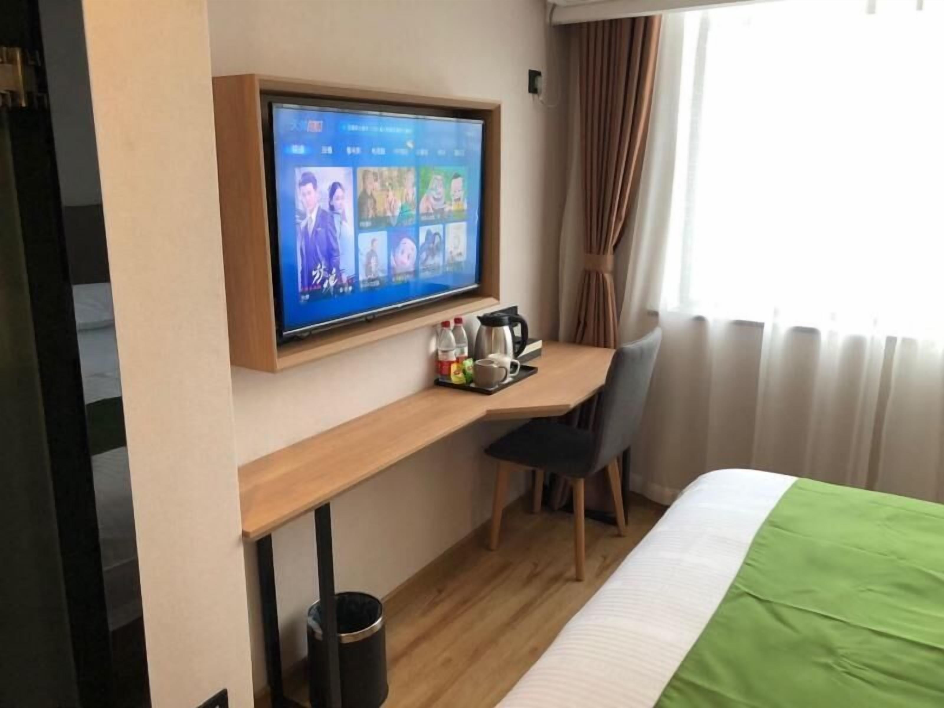 Una camera d'albergo con un letto, una scrivania con un monitor del computer, una sedia e una finestra con tende.