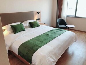 A neatly made bed with a green accent, a chair, and a small table in a hotel room.
